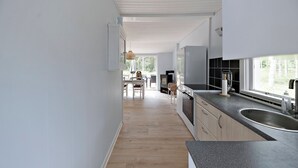 A modern kitchen with a large window, wooden flooring, and a dining area in the background. - Charmantes Sommerhaus in der Nähe eines fantastischen Sandstrandes (Åkirkeby)