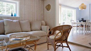 A room with a sofa, wicker chair, glass coffee table, and a dining area with a table and chairs. - Charmantes Sommerhaus in der Nähe eines fantastischen Sandstrandes (Åkirkeby)