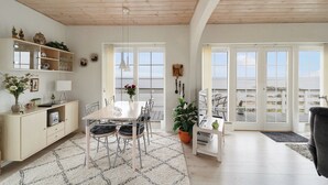 Eine moderne Küche mit weißen Schränken, einem Esstisch mit Stühlen, einem großen Fenster und Blick ins Freie.