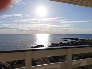 Vista costera con cielo despejado, un sol brillante reflejándose en el agua y terreno rocoso.