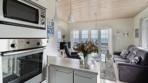 Eine Küche mit integriertem Mikrowellenherd, ein Essbereich mit Tisch und Stühlen sowie ein Wohnzimmer mit Sofa und Zierkissen.