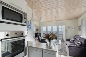 Una cocina con microondas incorporado, un comedor con mesa y sillas, y una sala de estar con sofá y cojines decorativos.