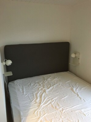 Ein Einzelbett mit dunklem Kopfteil, einer weißen Nachttischlampe und einer Wandleuchte.