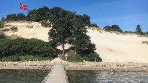 En træbro der fører til en sandstrand med et flag på en flagstang.