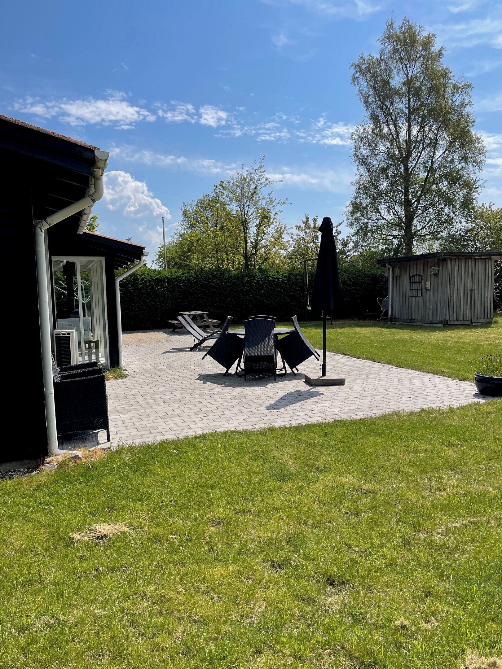 An outdoor patio area with a covered seating area, a small shed, and a grassy lawn.