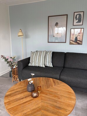 A living room with a dark grey sofa, striped pillows, a round wooden coffee table, and framed artwork on the wall. - Summer house near the sea and good experiences (Børkop)