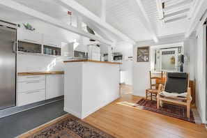 A modern kitchen with white cabinetry, a wooden island, and a dining area with a chair and rug.