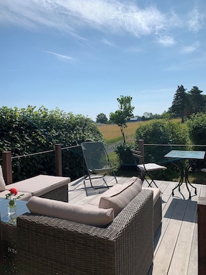 A patio with wicker furniture, a glass table, and a view of the countryside.