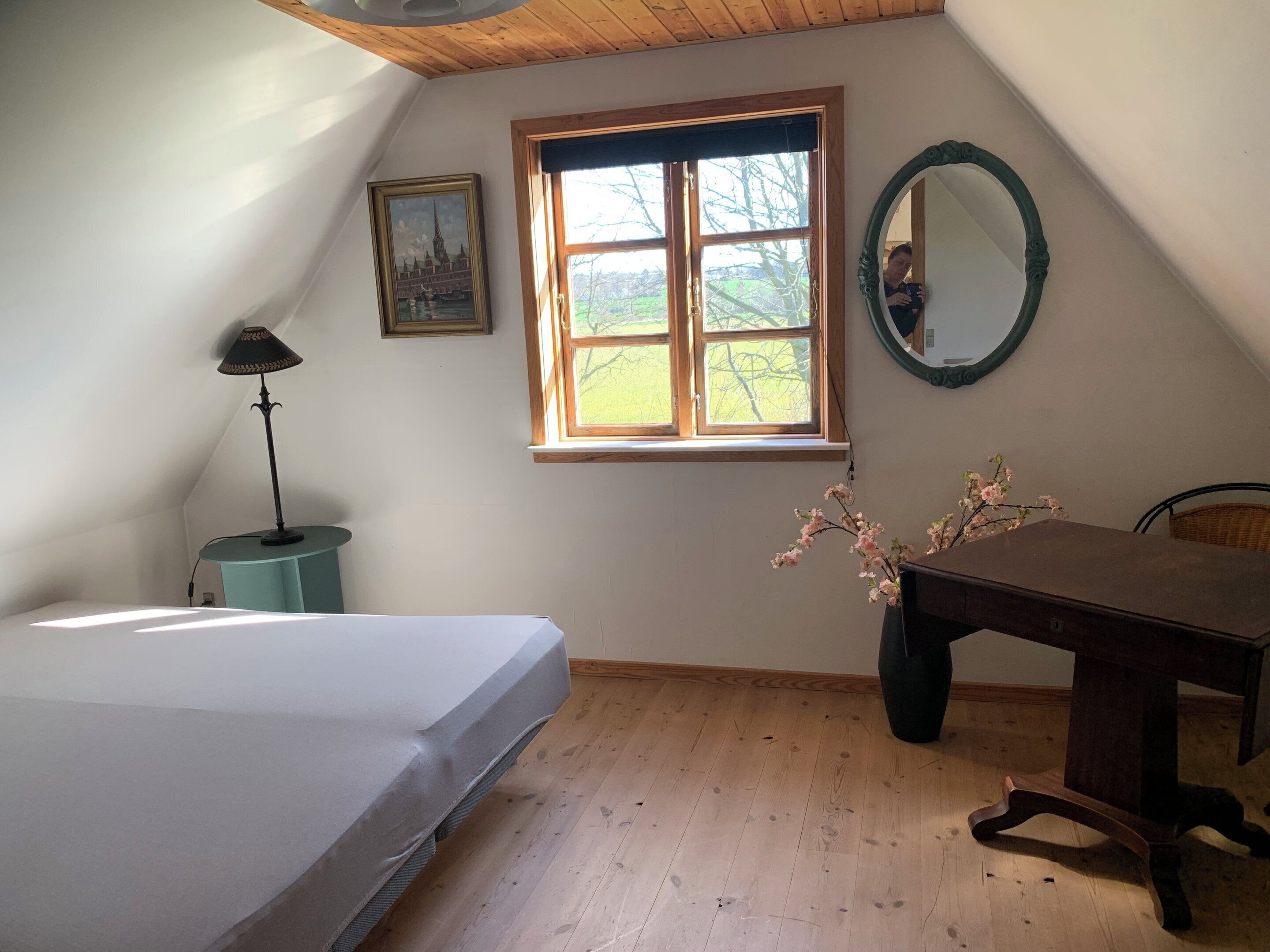 A bedroom with a bed, a desk, a chair, a window, a lamp, and a mirror.