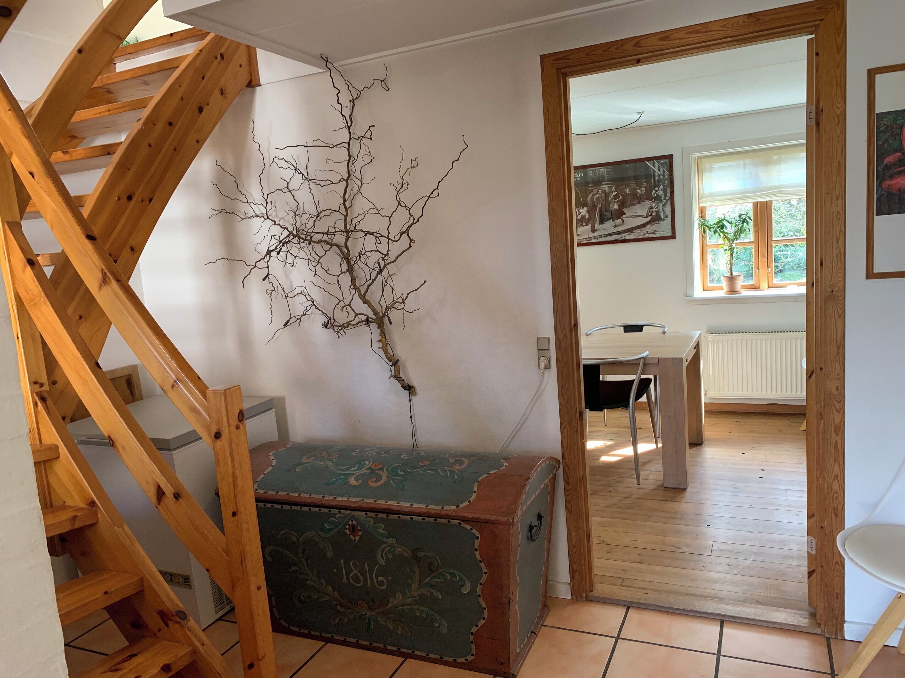 En trappe med et trægelænder, en vægmonteret grenskulptur og en antik kommode.