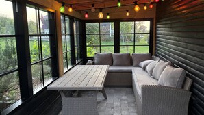 A covered patio with a wicker sofa, a table, and string lights. - Nice summer house with sea view (Jægerspris)