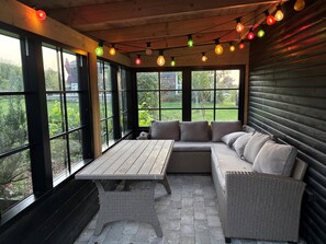 A covered patio with a wicker sofa, a table, and string lights.