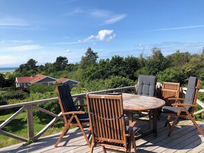 Eine Holzterrasse mit einem runden Tisch und vier Stühlen, mit Blick auf eine üppige Landschaft mit Bäumen und einem Gebäude in der Ferne.