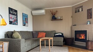 A cozy living room with a grey sofa, a small wooden table, a fireplace, and wall-mounted air conditioning. - Nice summer house with sea view (Jægerspris)