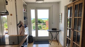 A kitchen with a wooden floor, a small round table, and a view through the door. - Nice summer house with sea view (Jægerspris)