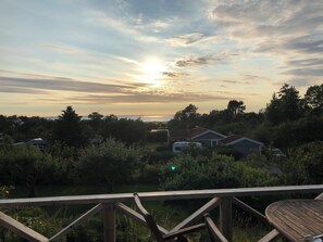Ein Sonnenuntergangsblick von einer Terrasse mit Holzgeländer, mit Blick auf eine Wohngegend mit Häusern und Bäumen.