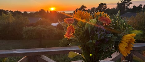 A sunset view with a table featuring a vase of flowers, a glass, and a bowl of watermelon slices.