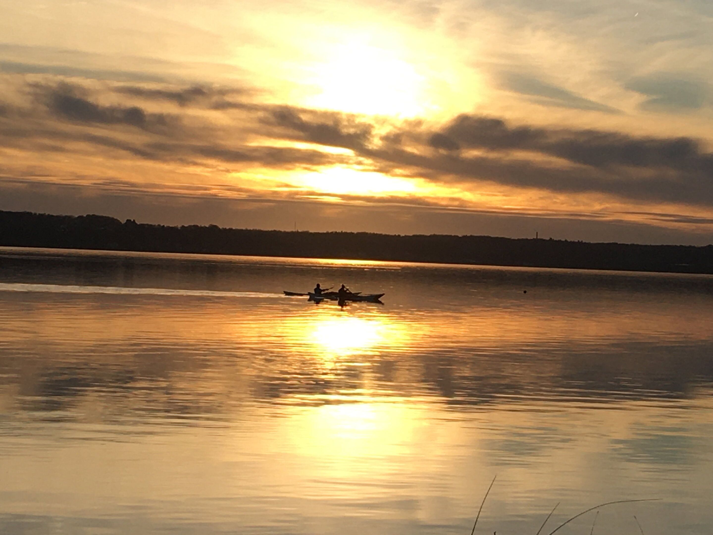 A calm lake at sunset with a silhouette of a boat and distant shoreline.