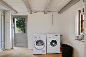 A laundry room with two white front-loading washing machines, a door leading outside, and a window with a shelf above it.