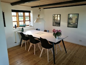 A dining area with a white table, black chairs, a vase of flowers, a hanging light fixture, and a window with a ship model.