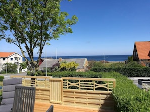 A wooden deck with a railing, a chair, and a view of the sea and buildings. - Lovely fishermans cottage with seaview (Allinge)