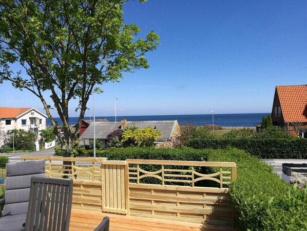 A wooden deck with a railing, a chair, and a view of the sea and buildings.