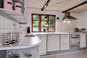 A modern kitchen with white cabinetry, a built-in oven, a dishwasher, and a window with a view of greenery.