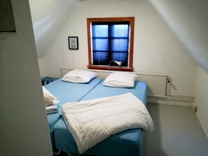 Ein kleines Zimmer mit einem Einzelbett, einem Fenster, einem Heizkörper und einem gerahmten Bild an der Wand.