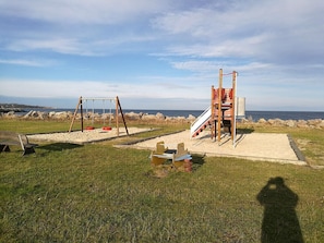 A playground with swings and a slide, set against a coastal backdrop.