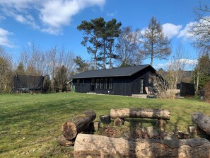 A black wooden building with a metal roof, surrounded by a grassy area and trees.
