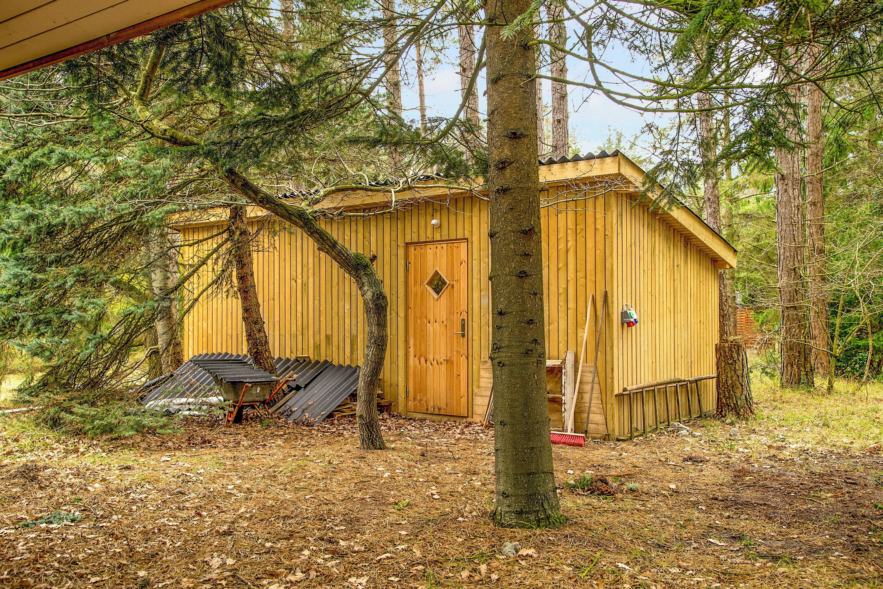 A wooden cabin with a door, surrounded by trees and a covered area with a roof.