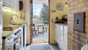 A compact kitchen with a built-in oven, a dining area with a table and chairs, and a brick wall. - Nice summer house in the middle of the forest (Store Fuglede)