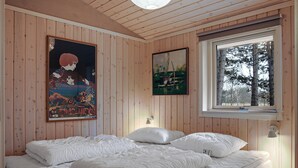 A room with wooden walls, a bed with white bedding, two paintings, and a window with a view of trees. - Nice summer house in the middle of the forest (Store Fuglede)
