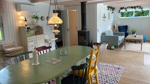 A dining area with a table, chairs, a hanging lamp, a bookshelf, a fireplace, and a view of the outdoors. - Idyllic summer house at the water's edge (Spøttrup)