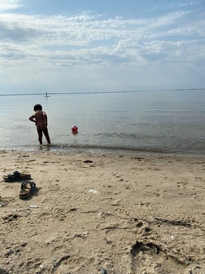 Una playa con huellas, un par de sandalias y una persona de pie en el agua.