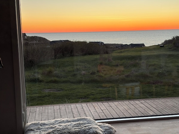 A view from a room with a large window overlooking a grassy area and a body of water during sunset.