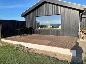 Ein modernes Gebäude mit einem großen Fenster, einer Holzterrasse und Gartenmöbeln.