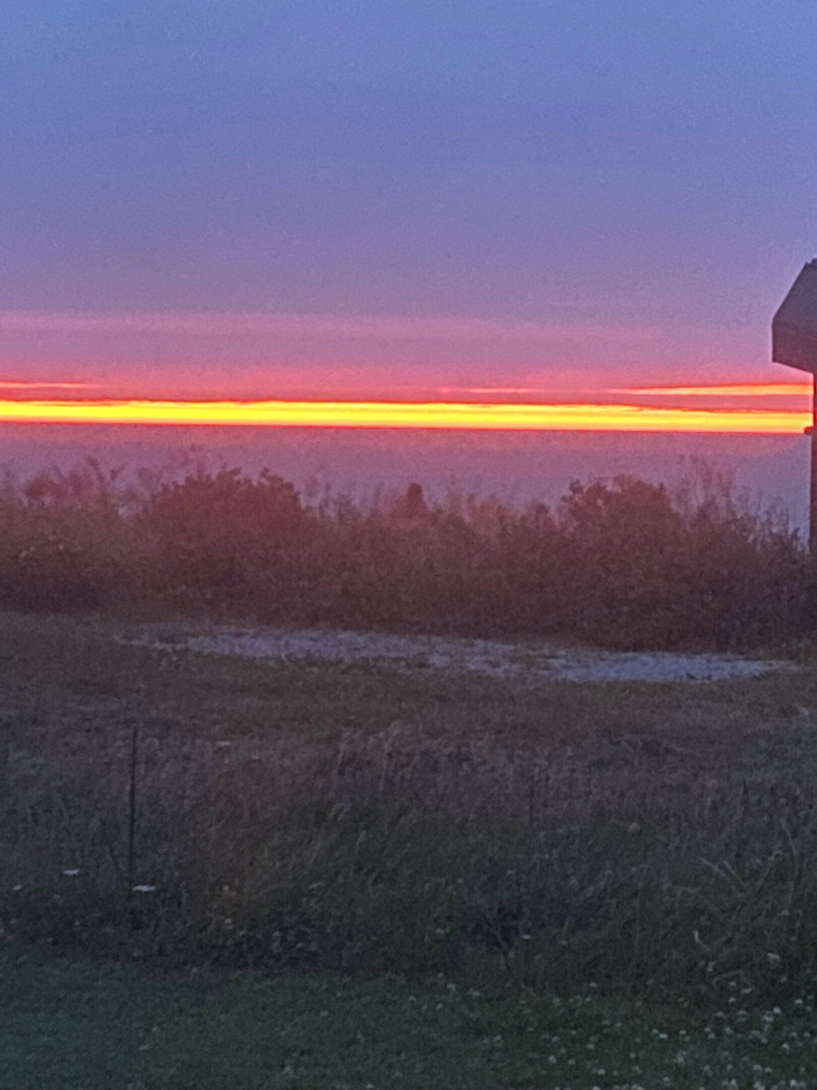 A sunset over a field with a road sign.