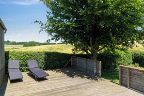 A wooden deck with two lounge chairs, a wooden fence, and a tree providing shade. - Lovely holiday home in idyllic surroundings (Rønne)