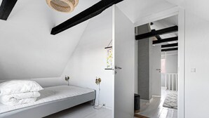 Una camera bianca con un letto, una porta che dà su un'altra stanza e un lampadario.