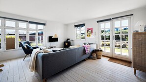 Ein modernes Wohnzimmer mit einer Couch, einem Sessel, einem Kamin und großen Fenstern.