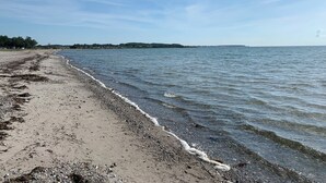 Ein Strand mit Kiesufer, ruhigem Wasser und blauem Himmel.