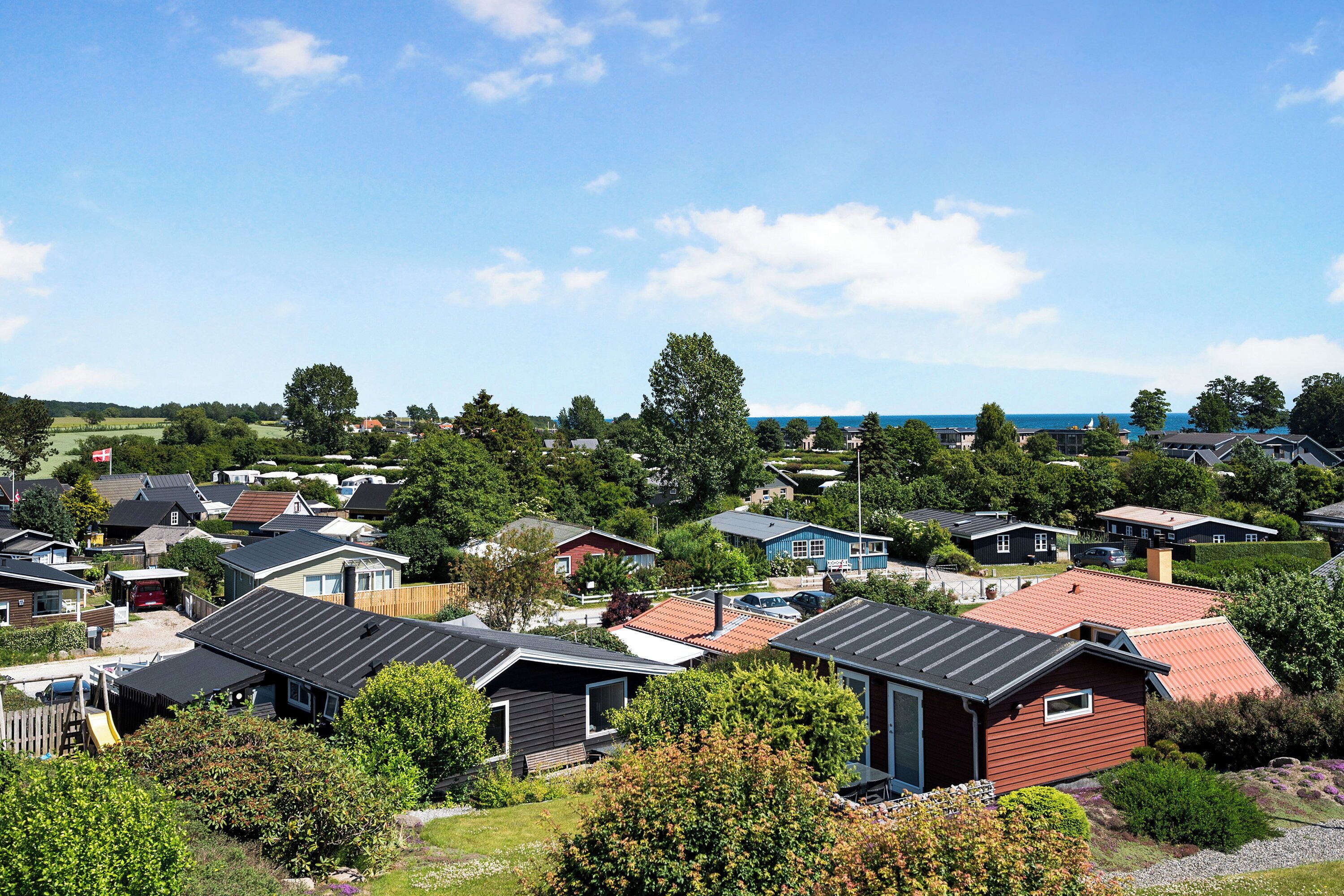 A residential area with multiple houses, some with sloped roofs, and a clear view of the sea in the background.