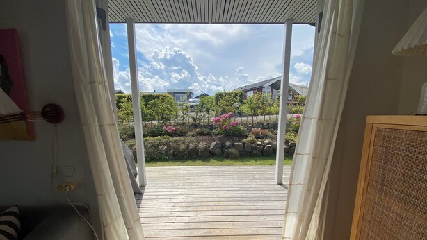 Eine offene Tür, die zu einer Holterrasse mit Blick auf einen Garten und Häuser in der Ferne führt.