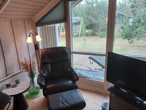 Una habitación con un ventanal grande, un sillón de cuero negro, una mesita con dos tazas y un televisor.