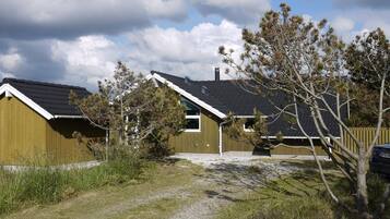 Et boligområde med to huse, hvoraf det ene har et skråt tag og skorsten, og det andet et fladt tag. En grussti fører hen til husene, og der er et træ i forgrunden.