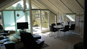 Una sala de estar moderna con televisor, asientos y un comedor con sillas y una mesa.