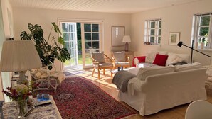 A spacious living room with a white sofa, a red throw blanket, a large plant, and a wooden floor. - Idyllically situated wooden house by the forest (Viborg)