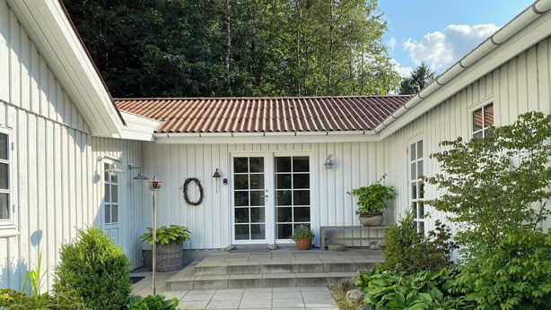 A white building with a tiled roof, a front door, and a small porch with potted plants. - Idyllically situated wooden house by the forest (Viborg)