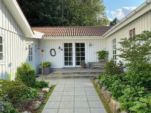 A white building with a tiled roof, a front door, and a small porch with potted plants.